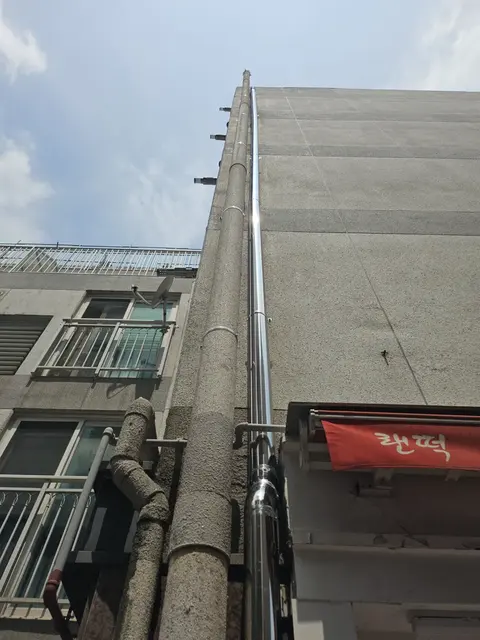 회색 패널 외벽 건물 우수관교체 후 올려다본 배관